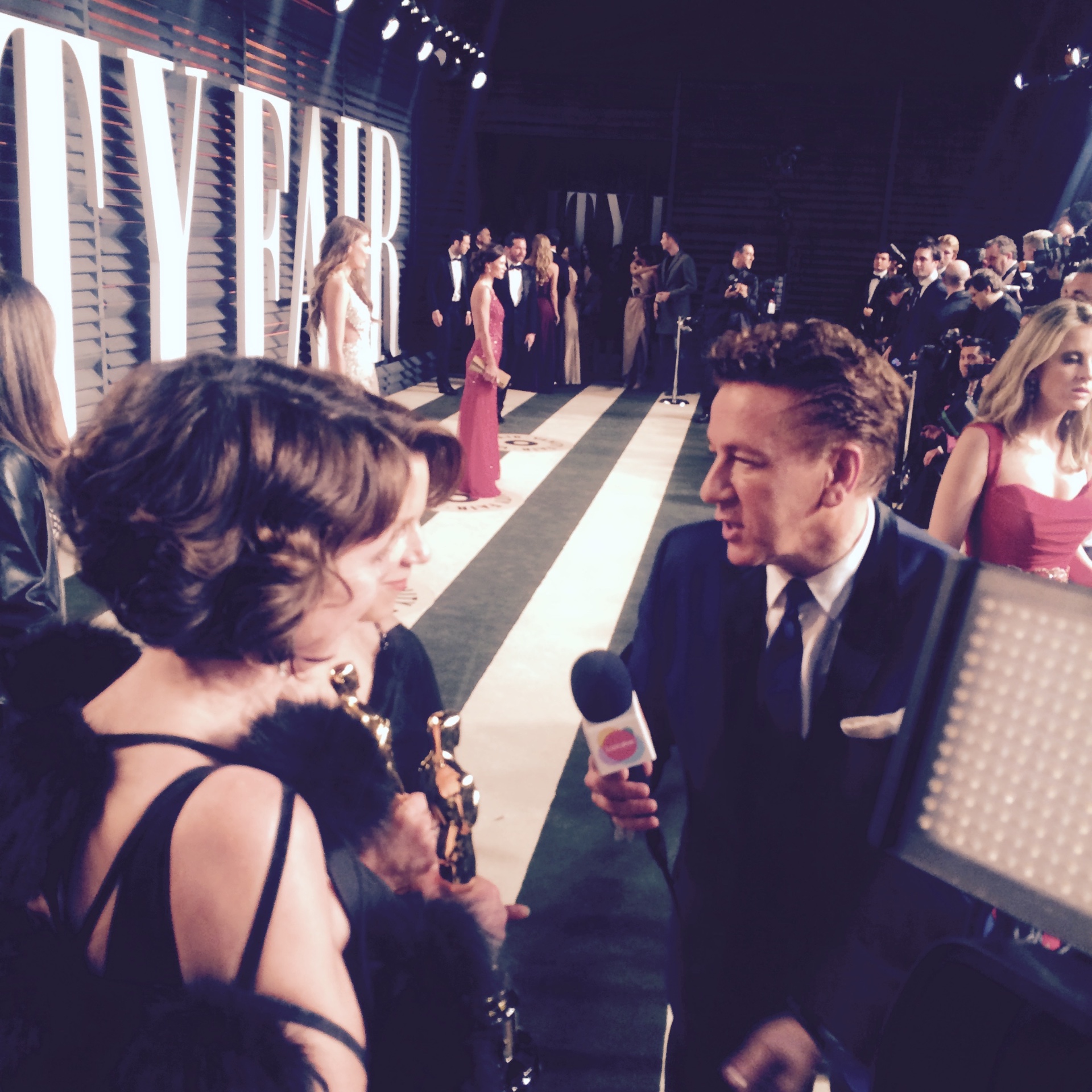 Oscar-winning filmmakers holding their statuettes give an on-camera interview on the Vanity Fair Oscar Party carpet.