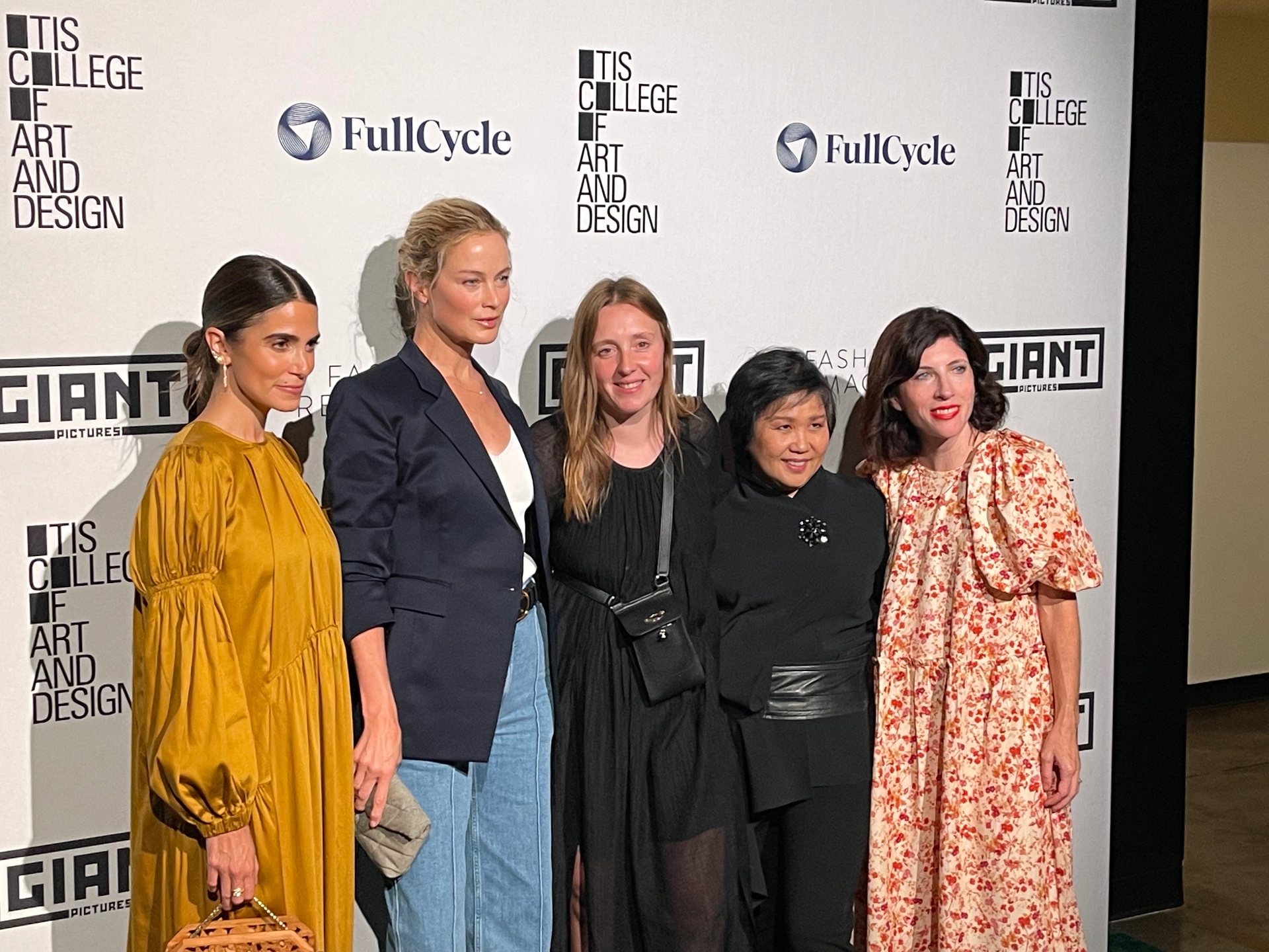 Five women pose together on the Fashion Reimagined red carpet in front of the sponsor step-and-repeat.