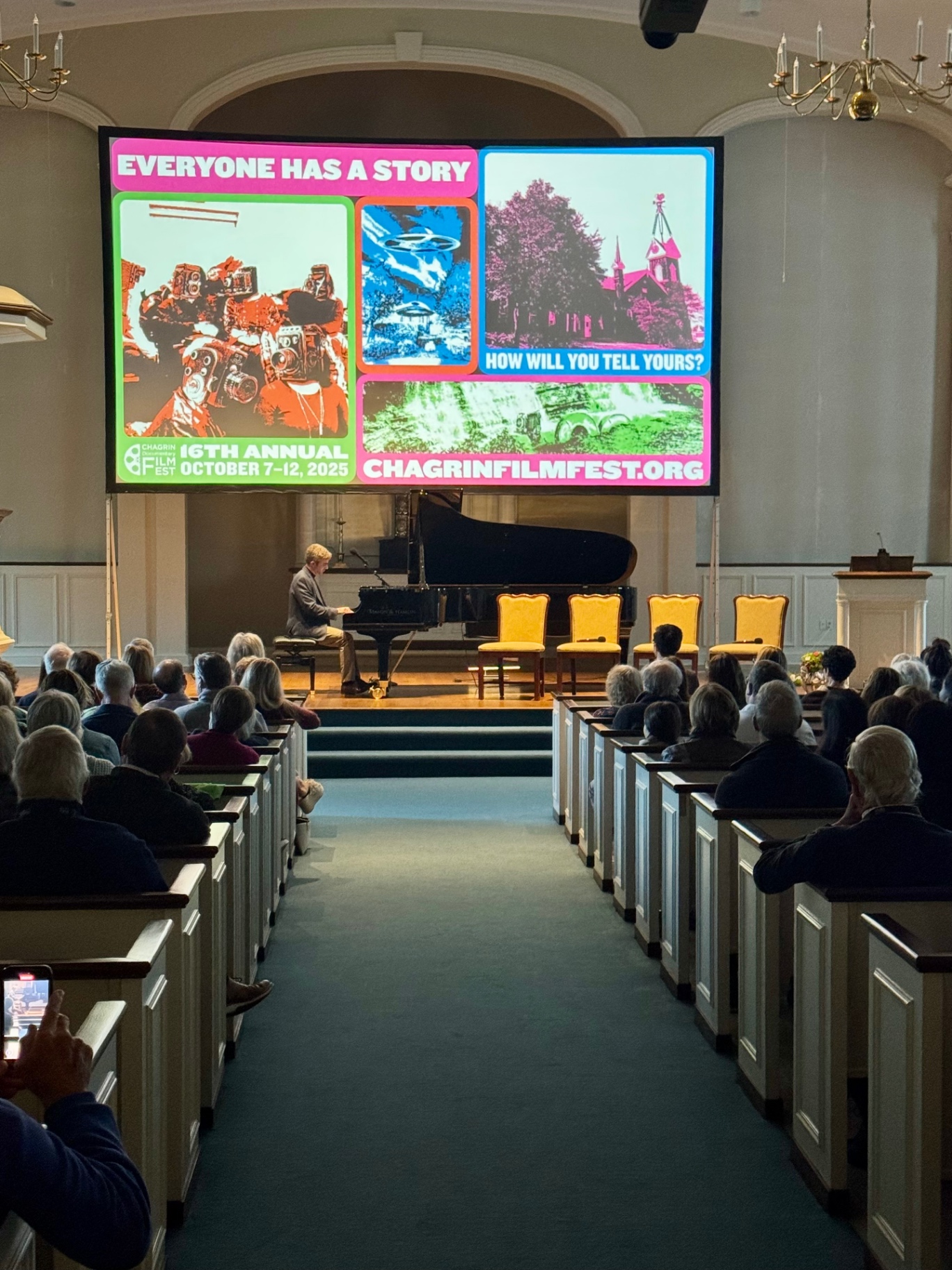 Audience at the Chagrin Documentary Film Festival watches a live piano performance beneath the festival's marquee screen.