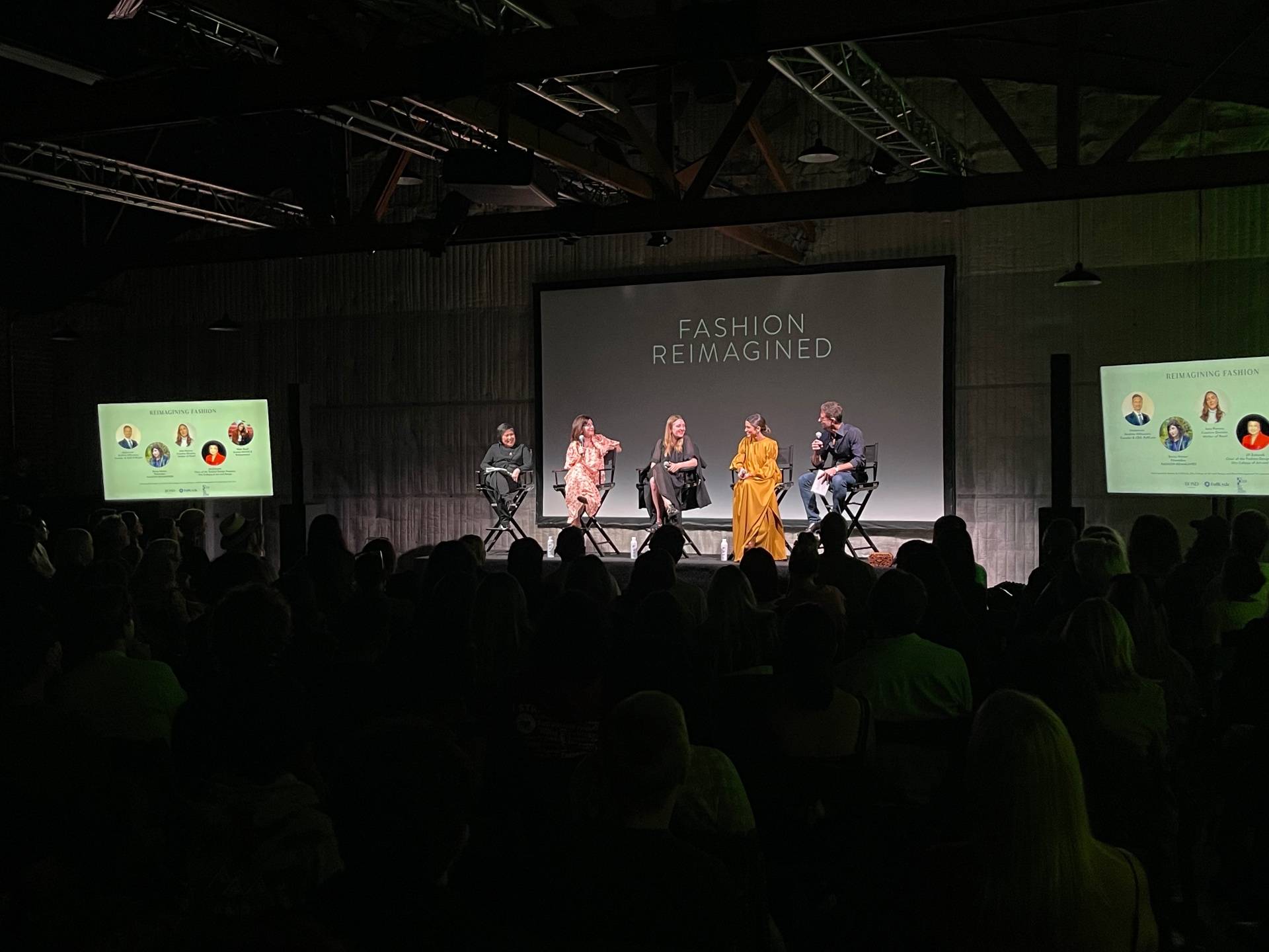 Wide stage shot of the Reimagining Fashion panel with title card and panelist headshot screens.