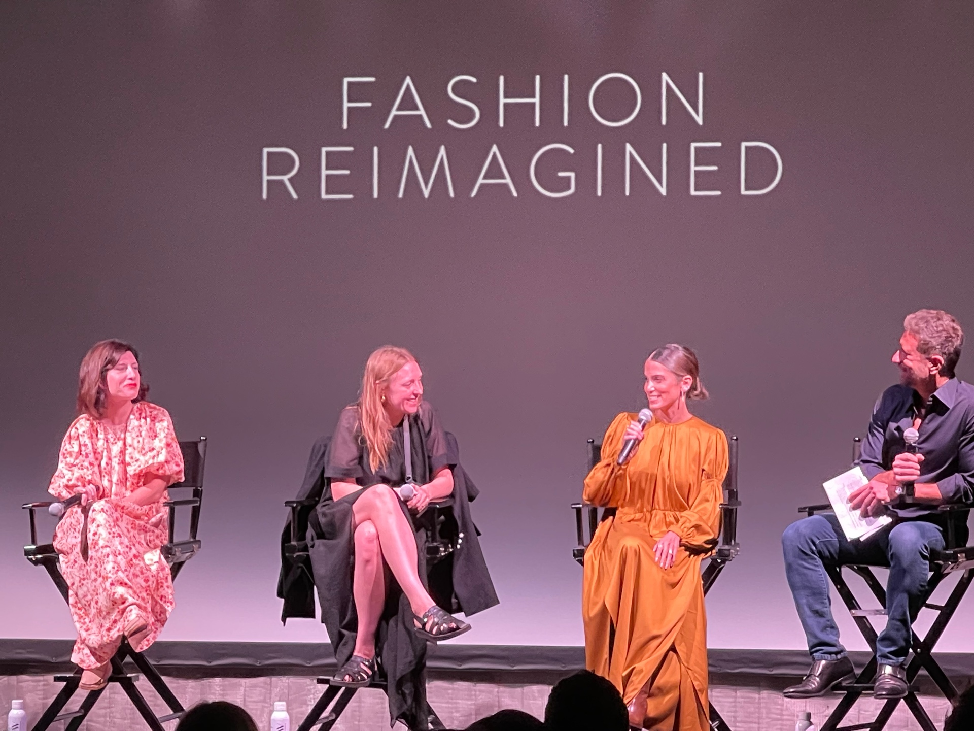 Tight stage shot of the Fashion Reimagined panel: subject, director, talent, and moderator in conversation.