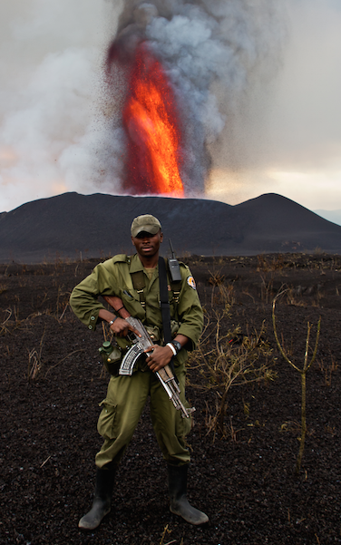 A Virunga park ranger standing in front of an erupting Nyiragongo volcano